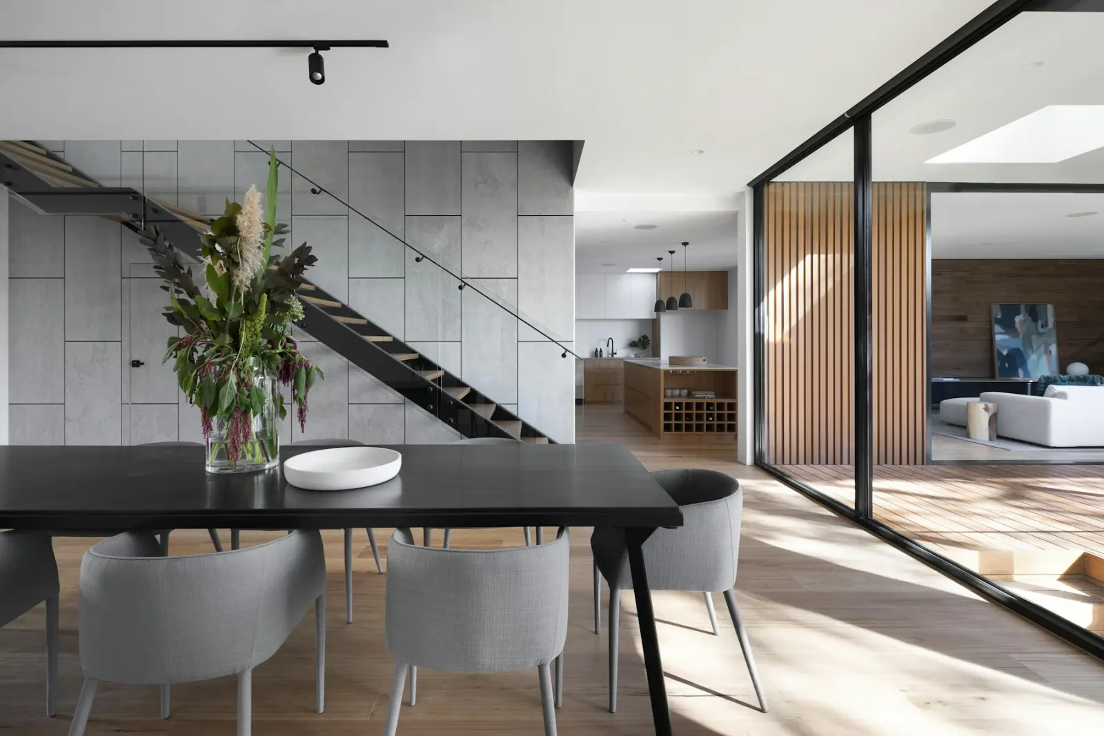 Modern dining room with a board-formed concrete feature wall and a black steel open-tread staircase — a modern hard-surface feature wall