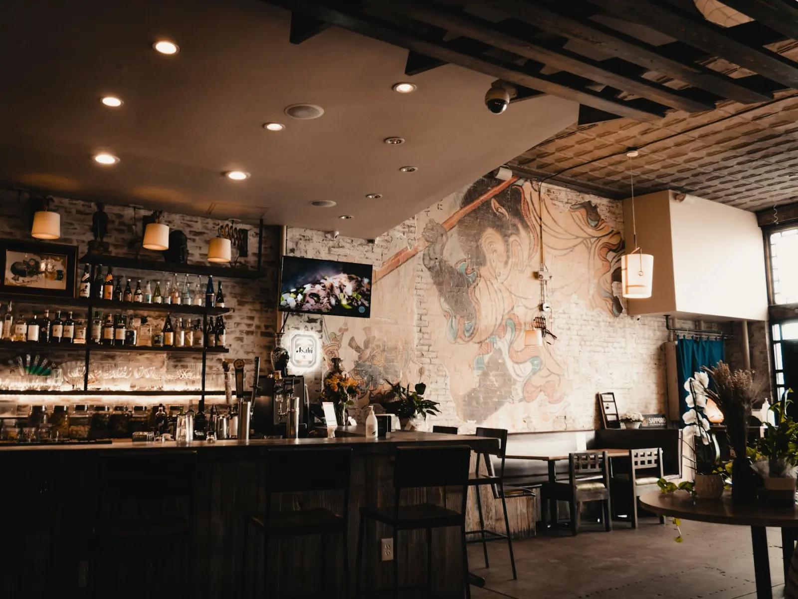 Dimly lit bar with a faded hand-painted mural on whitewashed exposed brick behind the counter — older building stock of the kind found across the region