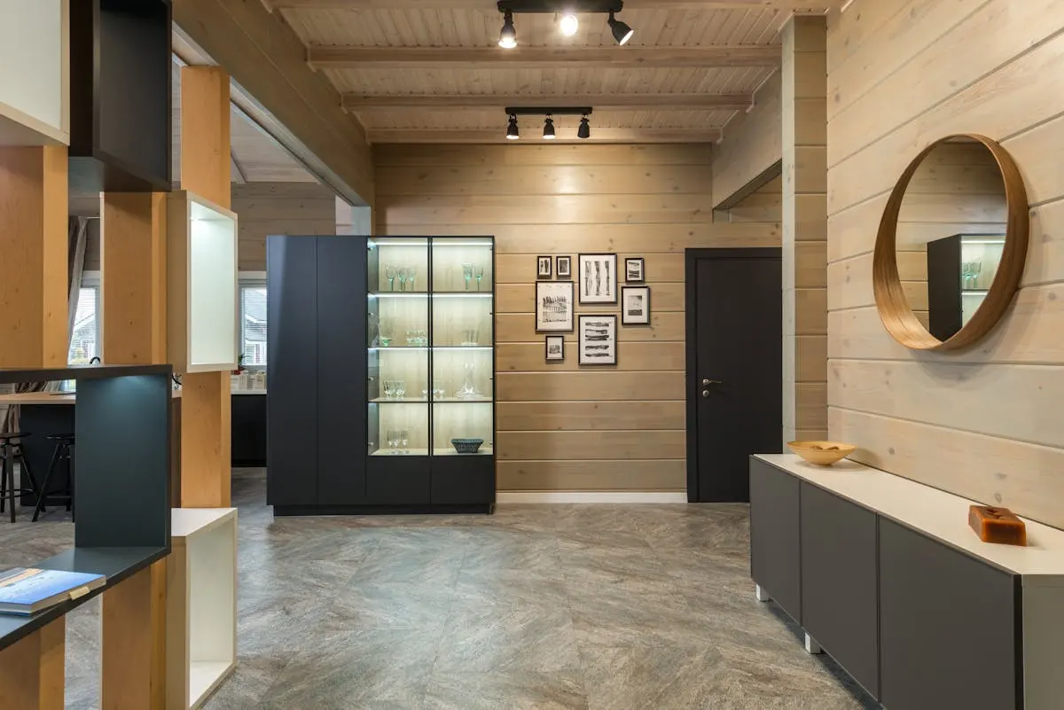 Wood-panelled hallway with a cluster of framed black-and-white prints, a round mirror and a dark storage unit — a panelled corridor using framed prints instead of a printed wall